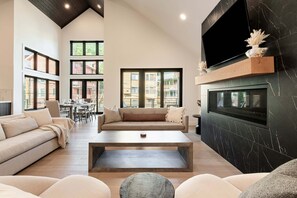 A spacious living room with a high ceiling, a large TV mounted on a black marble wall, and a cozy seating area with a sofa and a coffee table.