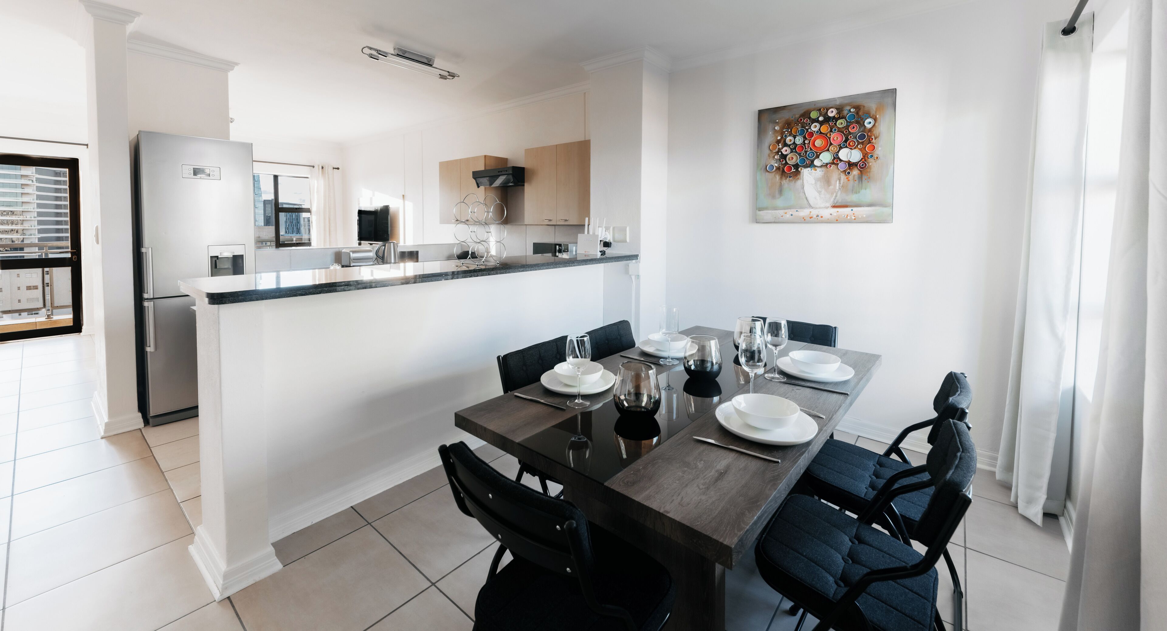 A modern kitchen with a dining area, featuring a large island, dark wooden table, and contemporary chairs.