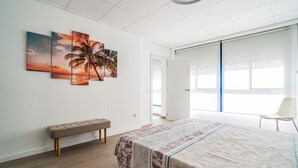 Un dormitorio con cama, una banca, un ventanal grande y una puerta que da a otra habitación.