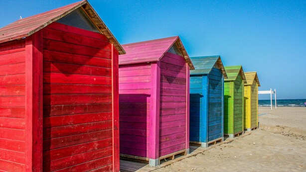 Una hilera de coloridas cabañas de madera a lo largo de una playa arenosa.