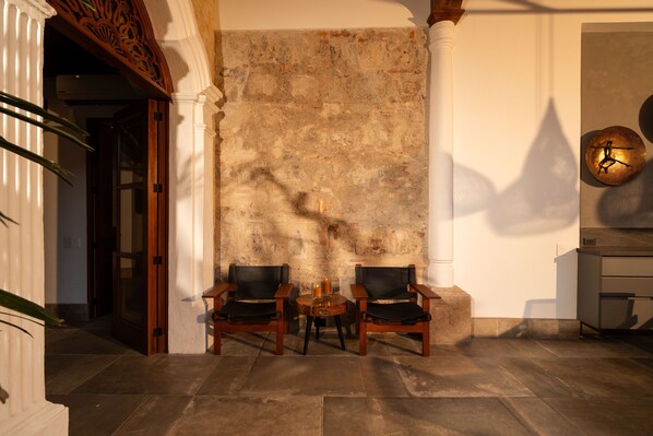A room with a stone wall, two wooden chairs, a small table, and a clock on the wall. - Singular Signature Residences (Antigua Guatemala)
