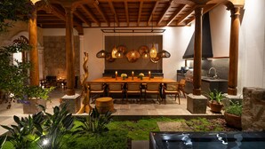 Comedor con mesa de madera, sillas, lámparas colgantes y pared de piedra.