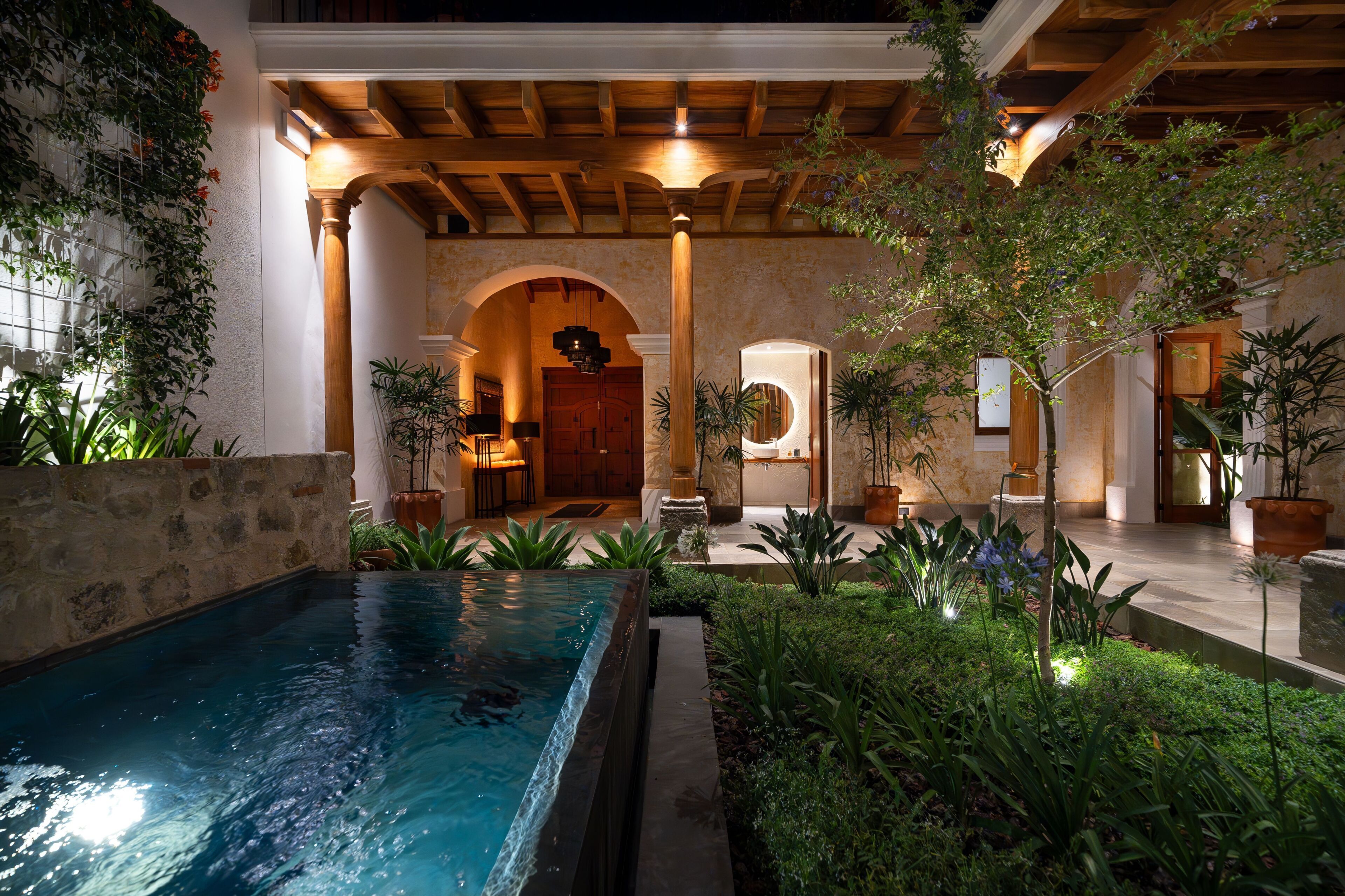A pool area with a wooden pergola, stone walls, and potted plants.