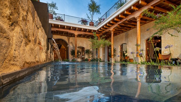 Una piscina con un muro de piedra y una pérgola de madera.