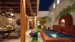 Un patio exterior acogedor con piscina, mobiliario de madera e iluminación colgante.
