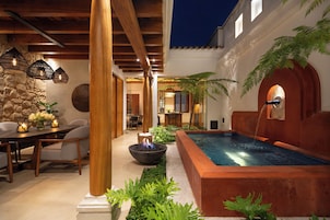 Un patio exterior acogedor con piscina, mobiliario de madera e iluminación colgante.