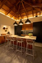 Una cocina moderna con vigas de madera, una isla de mármol, taburetes de bar e iluminación colgante.