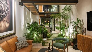 Una sala de estar moderna con una escalera que lleva a un nivel superior, rodeada de plantas de interior y una gran obra de arte enmarcada en la pared.