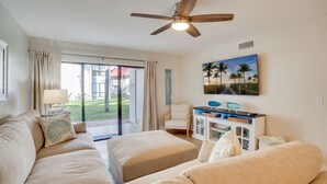 A spacious living room with a large sofa set, a ceiling fan, a TV on a white cabinet, and a sliding glass door leading to a patio.