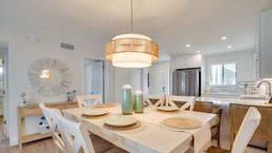 A modern kitchen with white cabinetry, a central island, and a dining area with a large table and chairs.