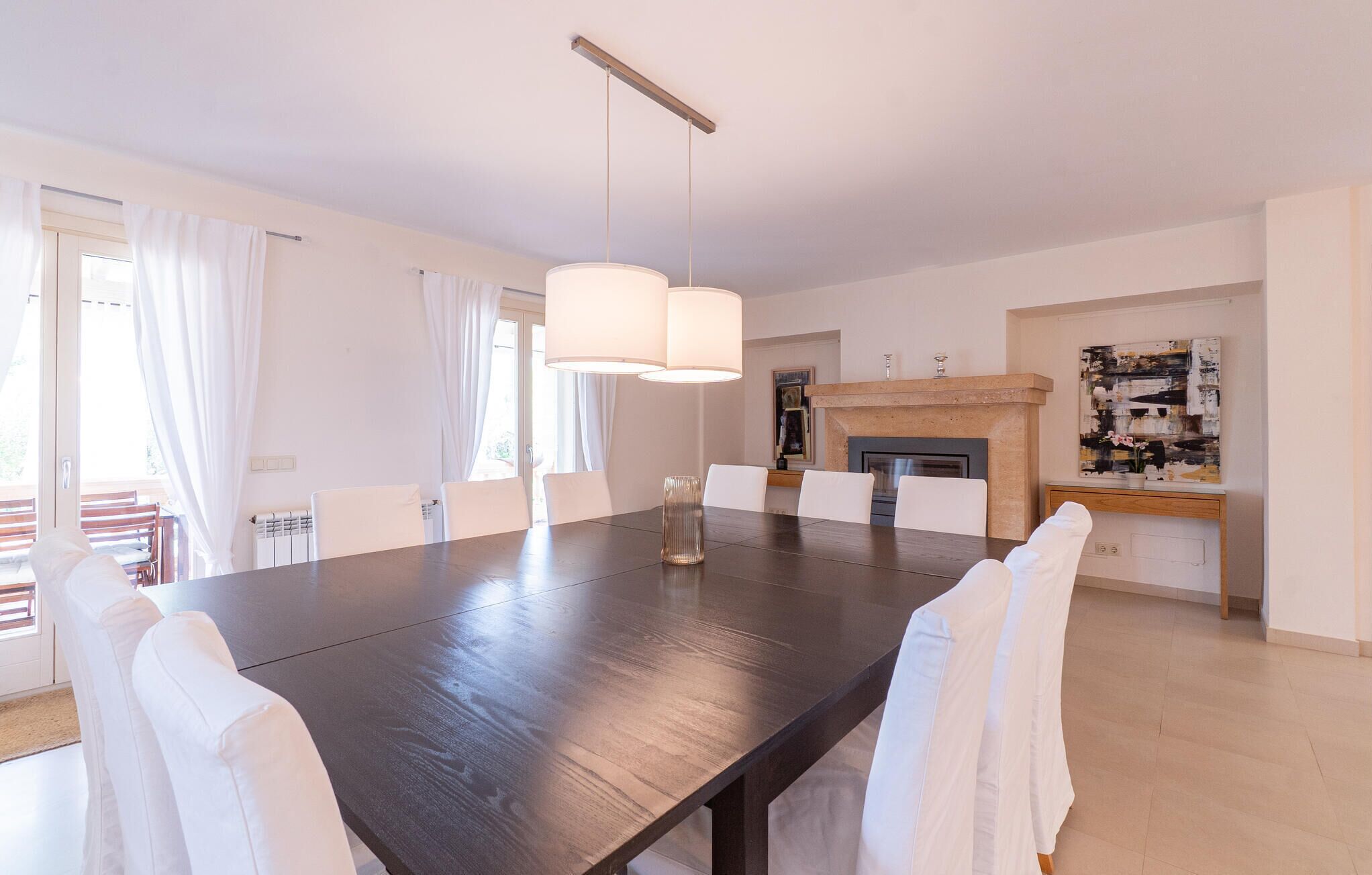 Un vaste espace dédié à la salle à manger, avec une grande table en bois foncé, des chaises blanches et un lustre moderne.