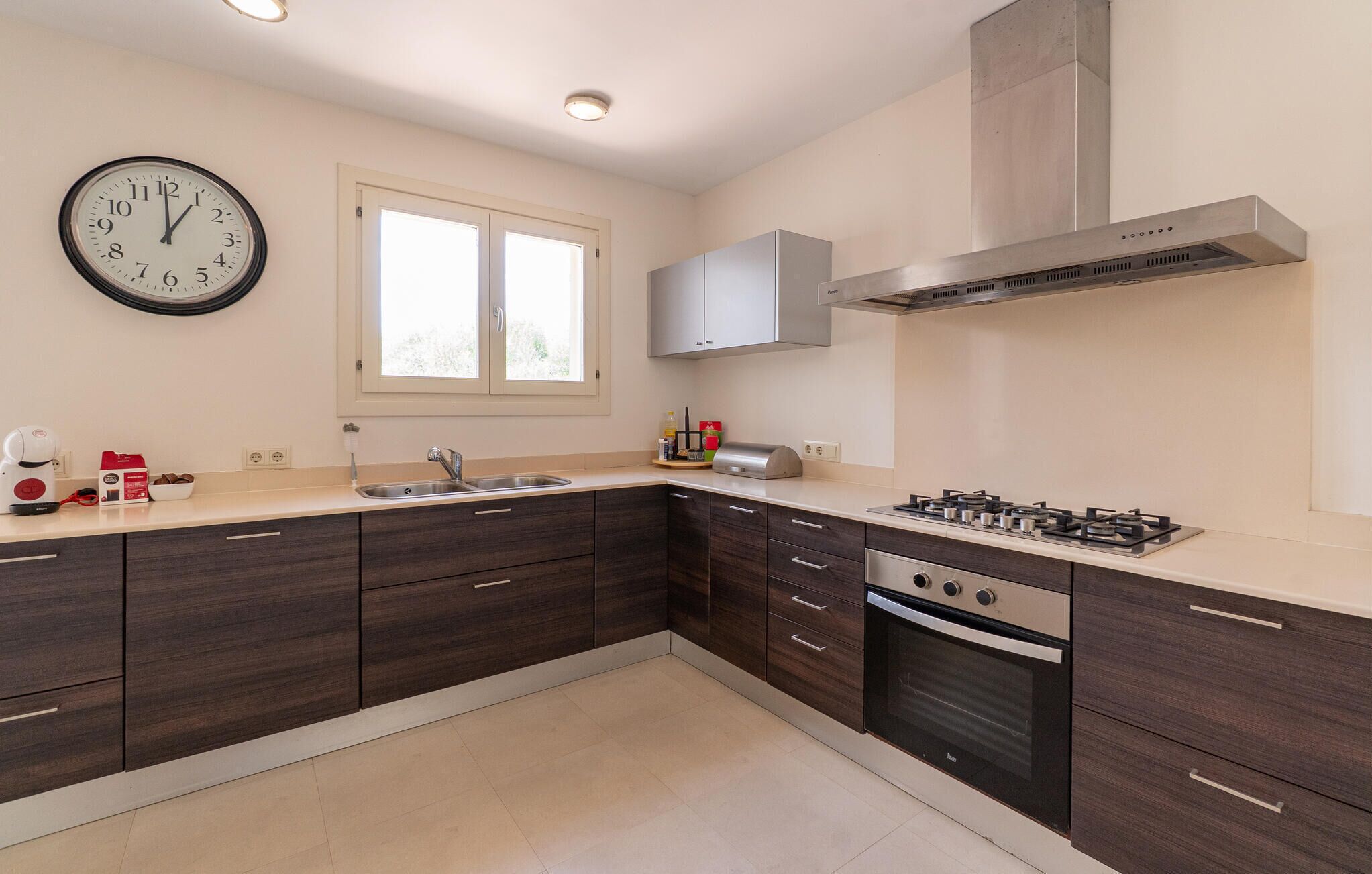 A modern kitchen with dark wood cabinets, a stainless steel range hood, and a built-in oven.