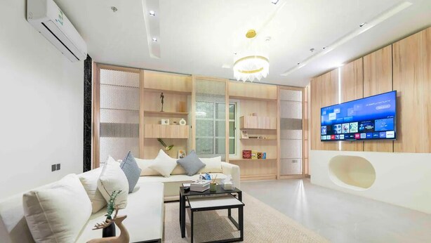 Een moderne woonkamer met een witte bank, een salontafel en een aan de muur bevestigde televisie.