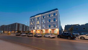 Een modern hotel met een meerlaags gebouw, een parkeerplaats met meerdere auto's en een heldere lucht.