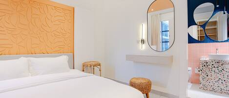 A modern hotel room with a large bed, a wall-mounted air conditioner, a round mirror, and a bathroom with a sink and tiled walls.