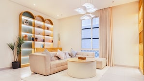 A modern living room with a beige sofa, a round coffee table, and a bookshelf with decorative items. - Two Bedroom Colorful & Exotic Flat in Alrabie (Riyadh)