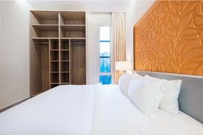 Une chambre d’hôtel dotée d’un grand lit, d’une armoire avec plusieurs étagères, d’une fenêtre offrant une vue agréable et d’un panneau décoratif mural.