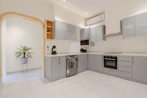 A modern kitchen with grey cabinets, a built-in oven, a washing machine, and a coffee maker. - Three Bedroom Colorful & Exotic Flat in Alrabie (Riyadh)