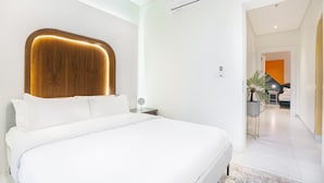 A modern hotel room with a large bed, a wooden headboard, a bedside table with a lamp, and a view into the adjacent room. - Three Bedroom Colorful & Exotic Flat in Alrabie (Riyadh)