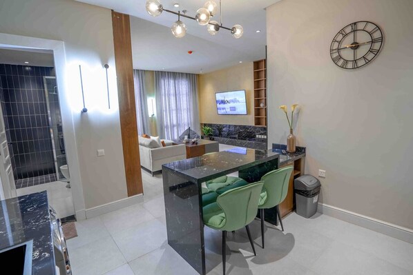A modern kitchen with a central island, green chairs, and a TV mounted on the wall.