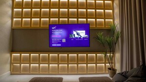 Una sala de estar moderna con un televisor de pantalla plana grande montado en la pared, iluminación empotrada, dos sofás y una planta en maceta.