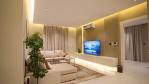 Een moderne woonkamer met een zithoek, een flatscreen televisie, een kamerplant en een bijzettafeltje.