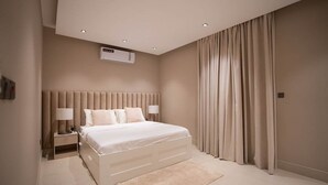 Een moderne slaapkamer met een groot bed, nachtlampjes, een airconditioning en een groot raam met gordijnen.