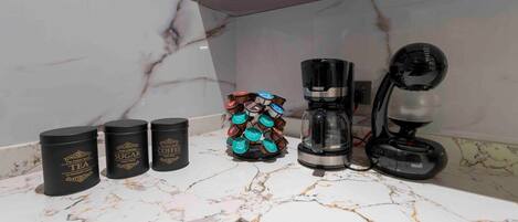 A kitchen counter with three black containers labeled 'TEA', 'SUGAR', and 'COFFEE', a coffee maker, and a coffee pod holder.