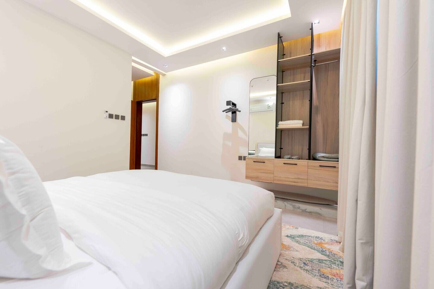 A modern hotel room with a large bed, a wooden wardrobe, a mirror, and a ceiling light.
