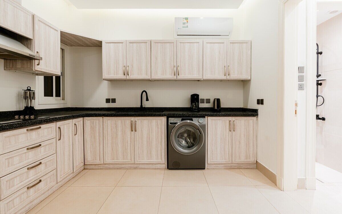 Una cocina moderna con armarios de madera clara, lavadora integrada y encimera negra.