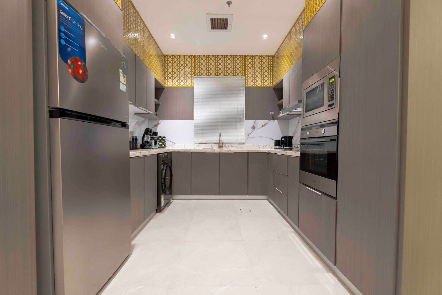 Una cocina moderna con gabinetes grises, horno empotrado y refrigerador de acero inoxidable.