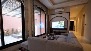 Uma sala de estar moderna com um sofá grande, uma TV de tela plana e vista para um pátio através de grandes janelas.