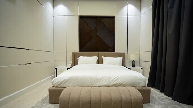 Quarto moderno com uma cama grande, mesas de cabeceira e um painel decorativo na parede.