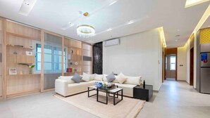 A modern living room with a sofa, coffee table, and decorative items. There is a wooden cabinet with shelves and a large window. - Stylish & Relaxing Flat in Alwadi Vll (Riyadh)