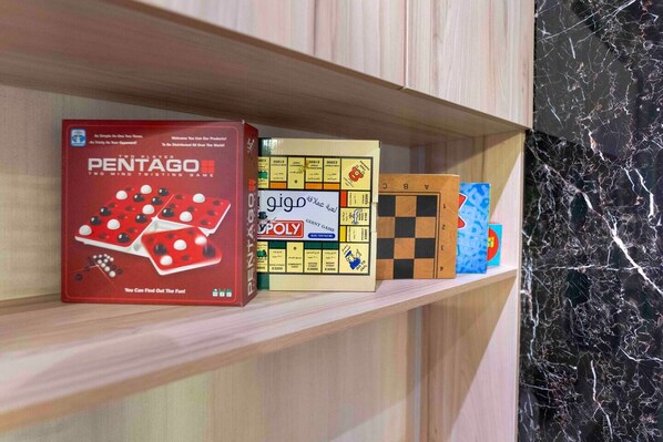 A shelf with various board games including Pentago, Monopoly, and a checkers set. - Trendy Apartment in Alwadi lX (Riyadh)