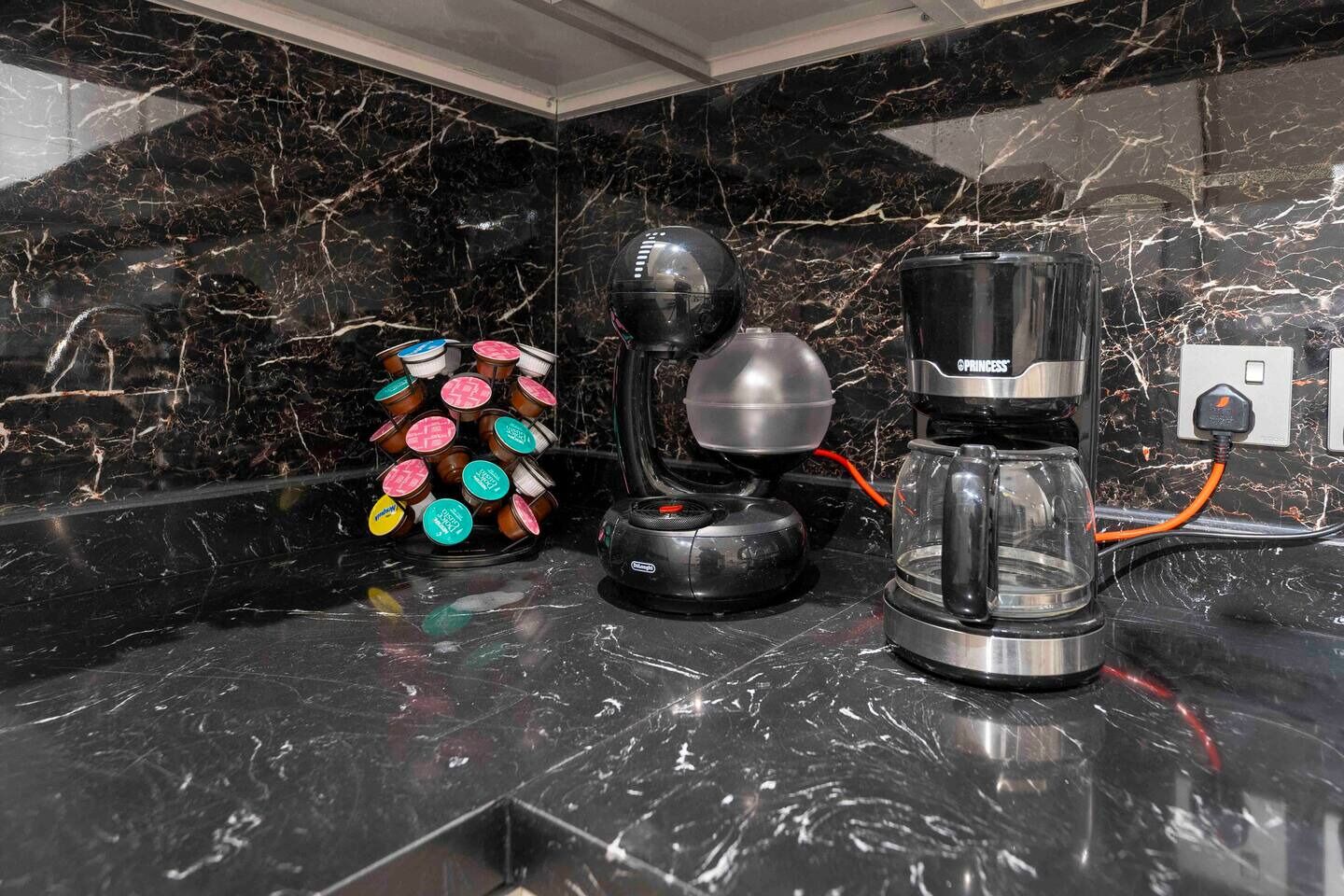 A kitchen counter with a coffee maker, a glass carafe, and a container of coffee pods.