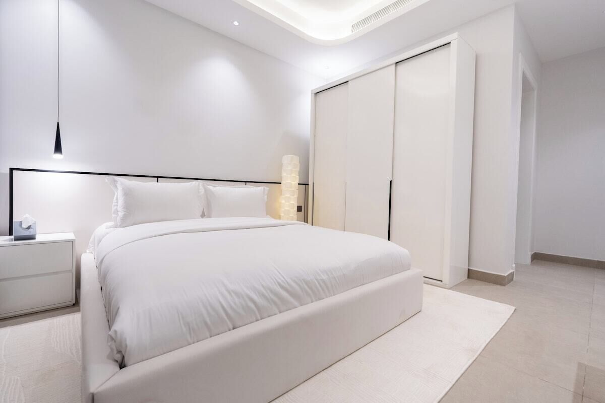 Un dormitorio moderno con una cama grande, una mesita de noche, un armario e iluminación en la pared.