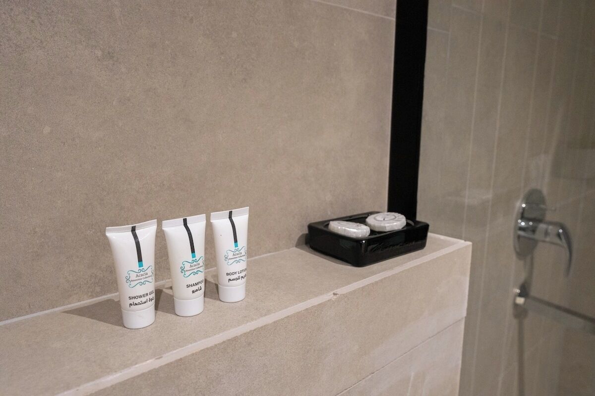 A bathroom shelf with three bottles of shower gel and two round containers, likely for body lotion or cream.