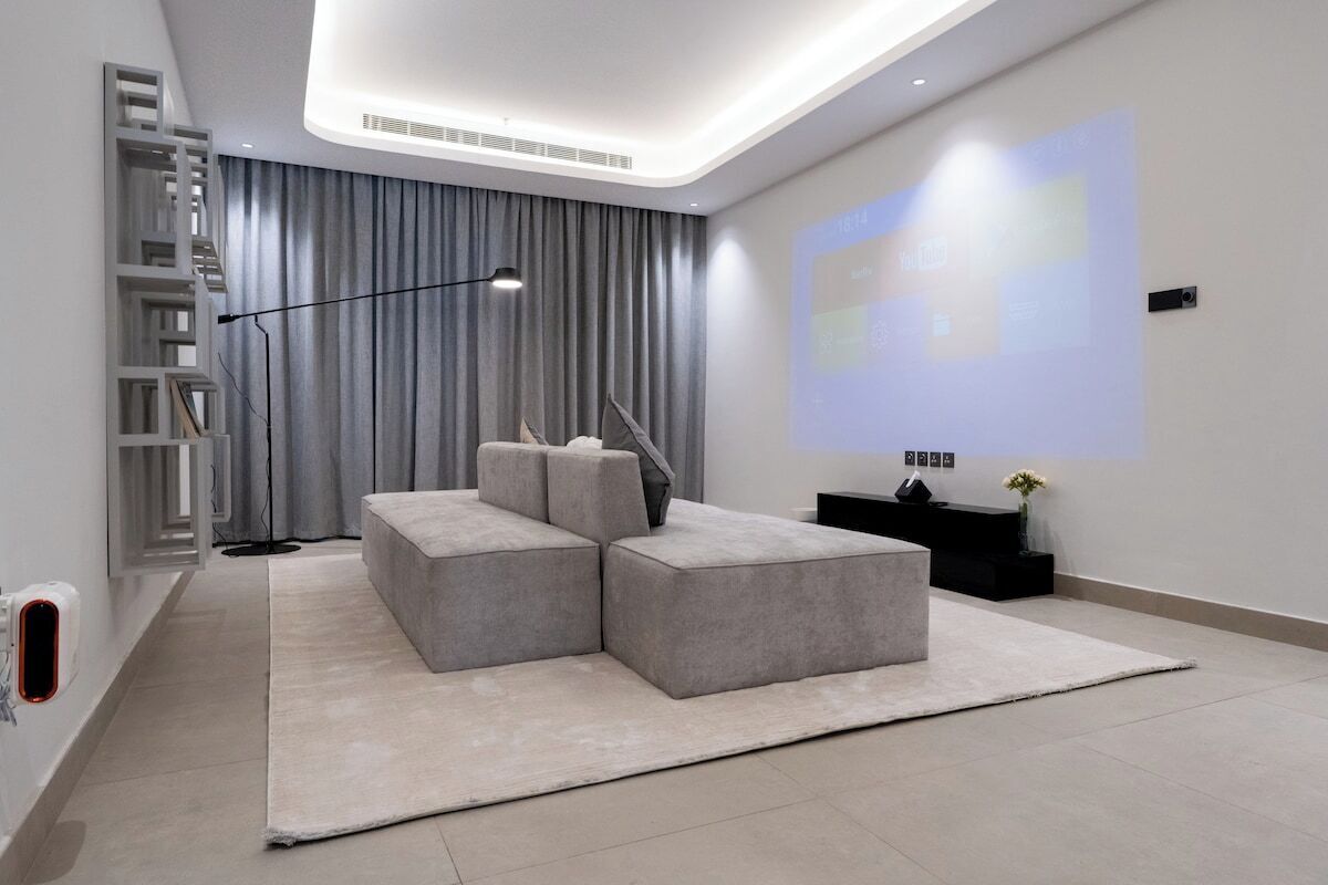 Ein modernes Wohnzimmer mit einem Ecksofa, einer Projektionsleinwand und einem minimalistischen Design.