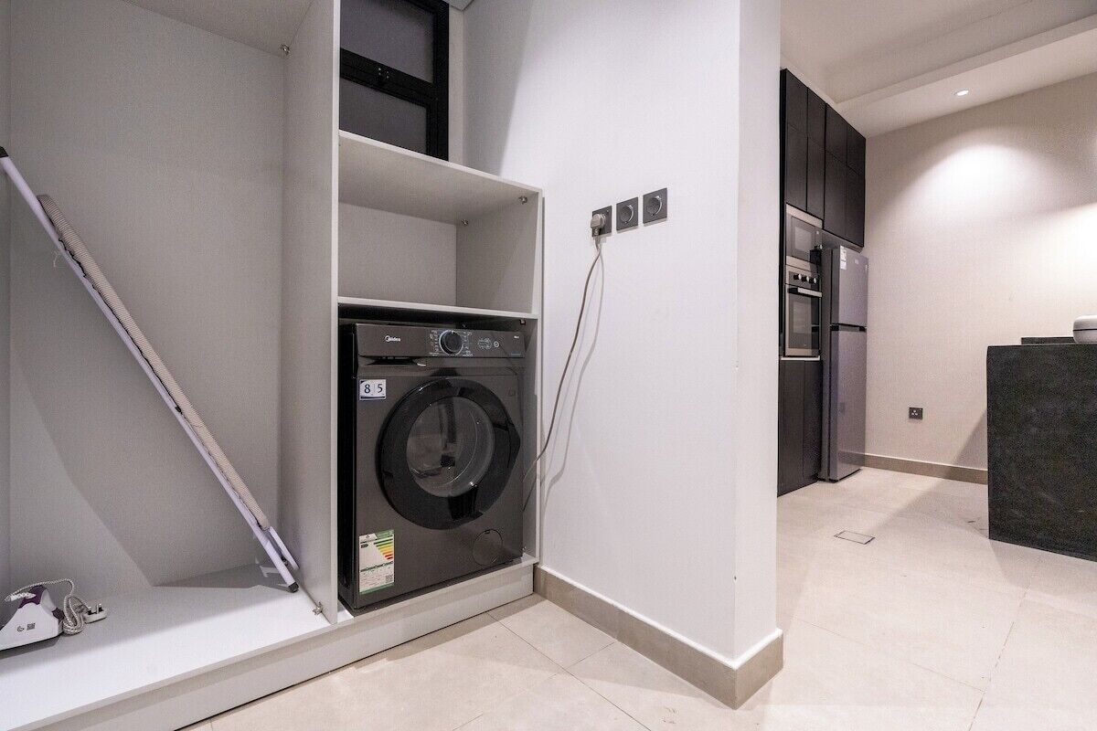 A compact kitchen with a built-in washer and dryer, a refrigerator, and a dark countertop.