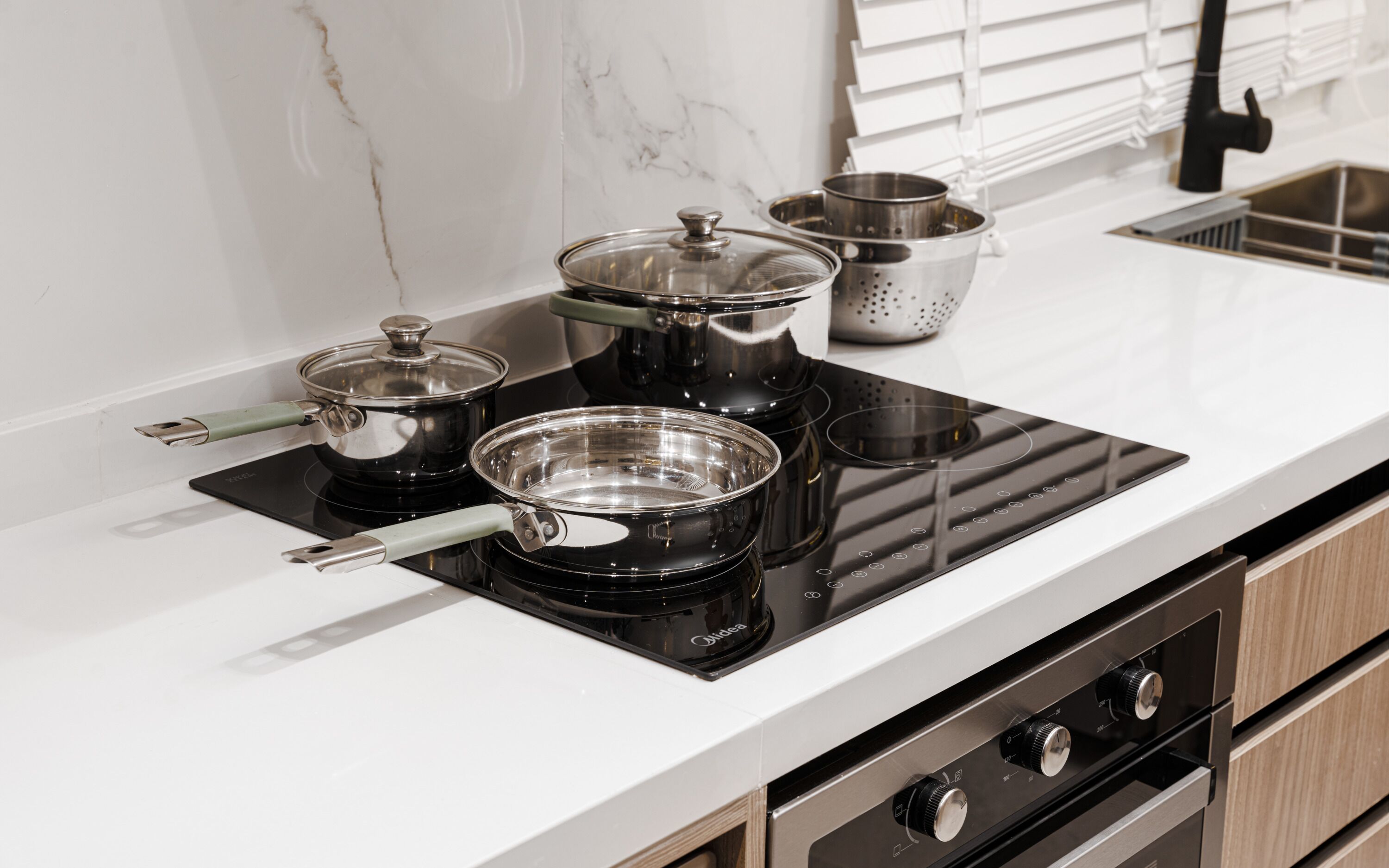 Una cocina moderna con una placa de inducción negra, ollas de acero inoxidable y un colador.