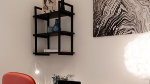 Een moderne werkruimte met een rode stoel, een zwart bureau, een laptop, een zwart wandrek met decoratieve objecten en een abstract kunstwerk aan de muur.
