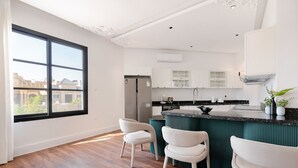 Een moderne keuken met witte kasten, een zwart aanrecht en een groen kookeiland. Er staan drie witte stoelen bij de eethoek.