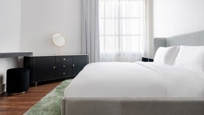 Een moderne slaapkamer met een bed, een dressoir, een ronde spiegel en een raam met dunne gordijnen.