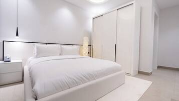 A modern bedroom with a large bed, a bedside table, a wardrobe, and a wall-mounted light fixture.