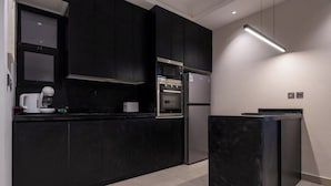 A modern kitchen with dark cabinetry, stainless steel appliances, and a marble island. - Trendy Apartment in Almohamadia (Riyadh)