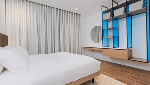 Una habitación de hotel moderna con una cama grande, un armario empotrado y un espejo redondo.