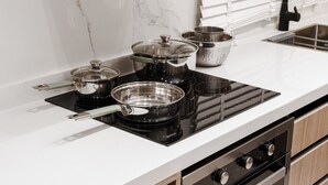 A modern kitchen with a black induction cooktop, stainless steel pots, and a colander. - One Bedroom Trendy Apartment in Almughrizat (Riyadh)
