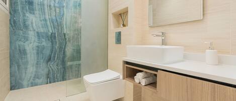 A modern bathroom with a marble wall, a white sink, and a toilet.