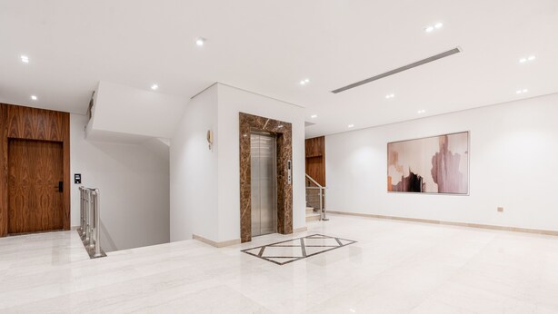 A spacious lobby with a marble floor, a wooden door, an elevator, and a large abstract painting on the wall. - One Bedroom Trendy Apartment in Almughrizat (Riyadh)